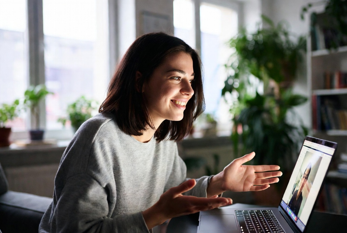 Attractive young woman having friendly conversation during live video call, smiling and gesturing naturally